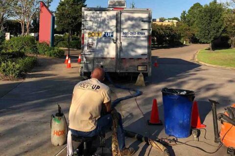 A worker operates equipment near a Poly Up truck, with hoses and cones set up on a street