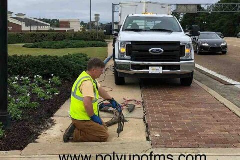 A man is kneeling next to a truck, engaged in an activity on the ground.